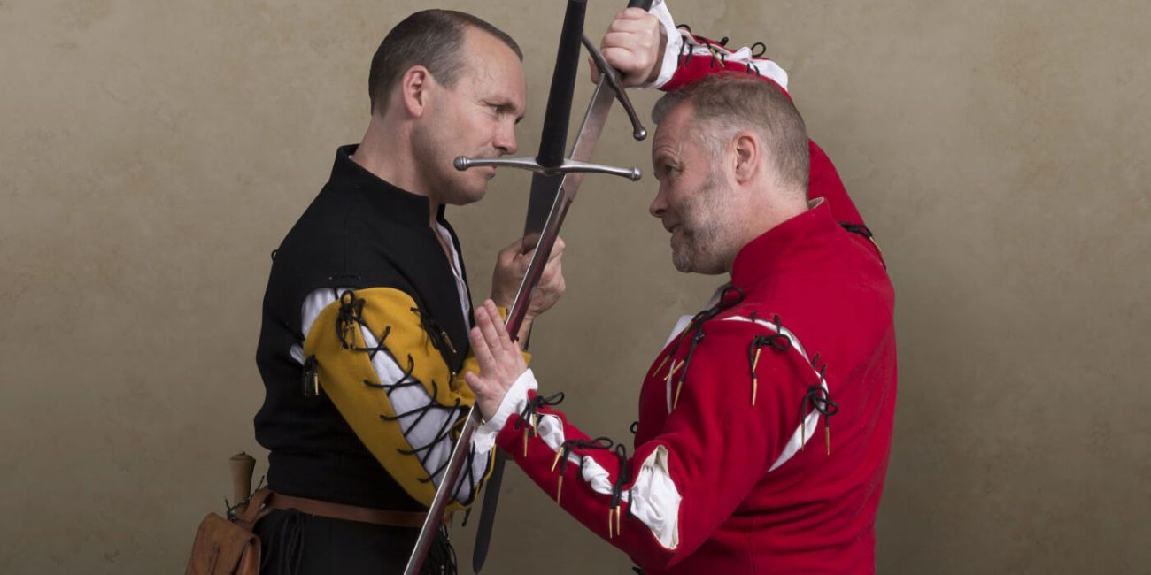 Two men in period costumes fighting with longswords