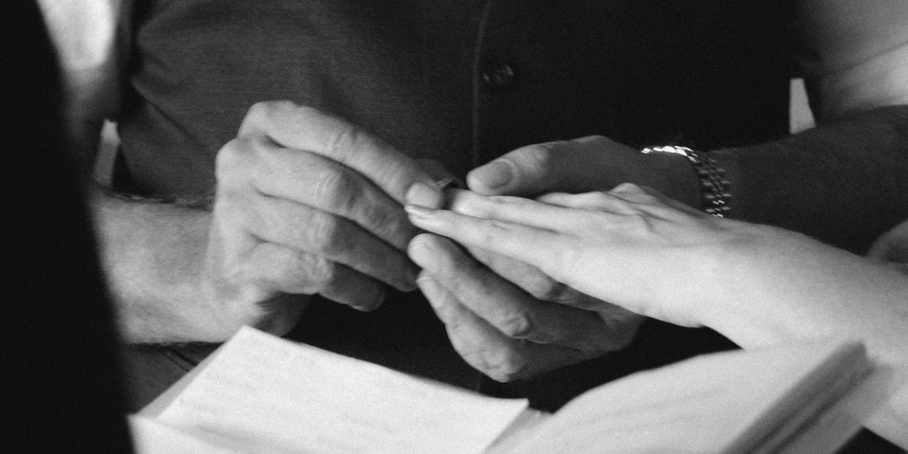 black and white close up picture of person placing a wedding ring on their partners finger