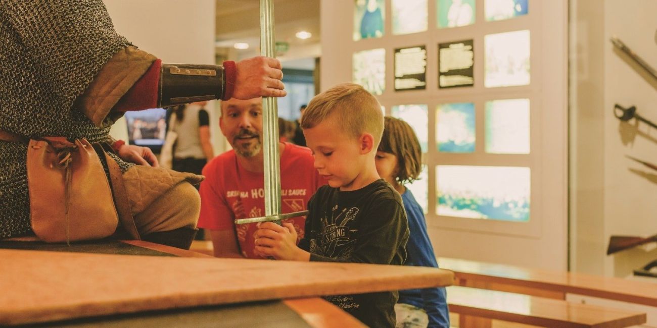 Museum staff member and child holding sword in an family activity at the museum