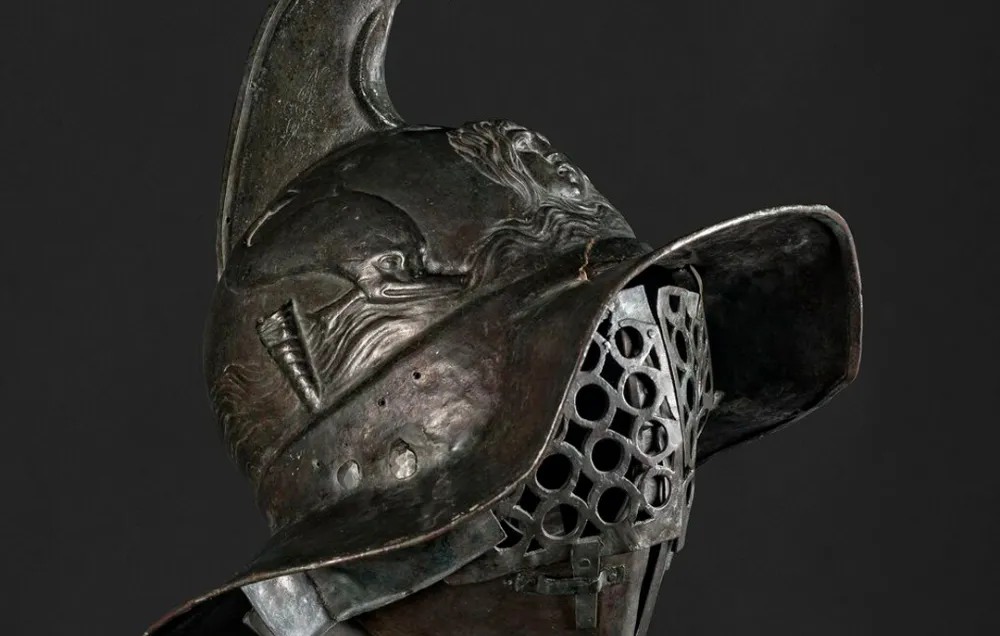 A dark metal helmet with a large griffin crest on top against a dark background