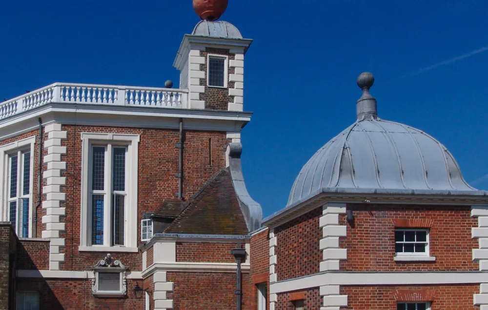 A colour photo of a red brick building with white stone decorations and a red ball on top