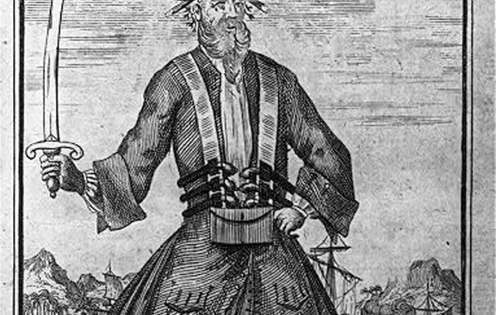 A black and white engraving of a bearded pirate holding a sword upright with lit matches in his beard.