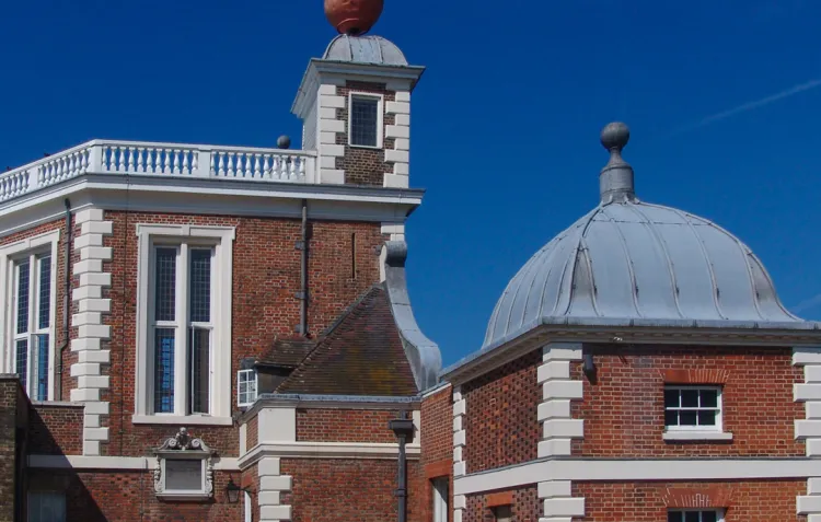 A colour photo of a red brick building with white stone decorations and a red ball on top