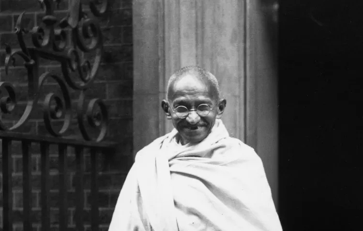 A black and white photograph of Mohandas Gandhi standing outside No.10 Downing Street wearing his familiar white robes.
