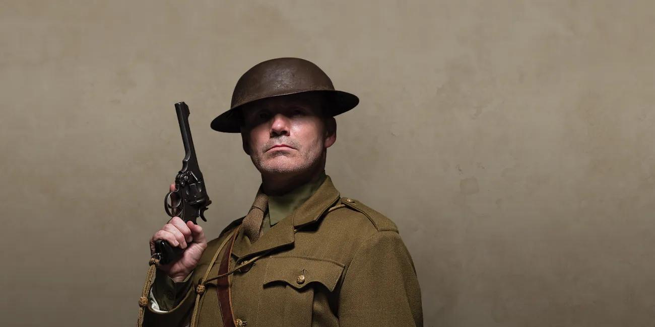 Man in khaki uniform and tin helmet holding a pistol