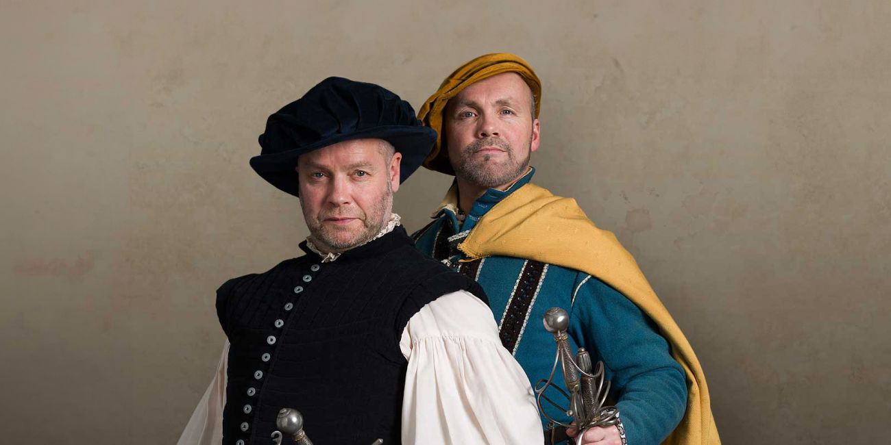 wo flamboyantly dressed Renaissance sword masters posing with their swords
