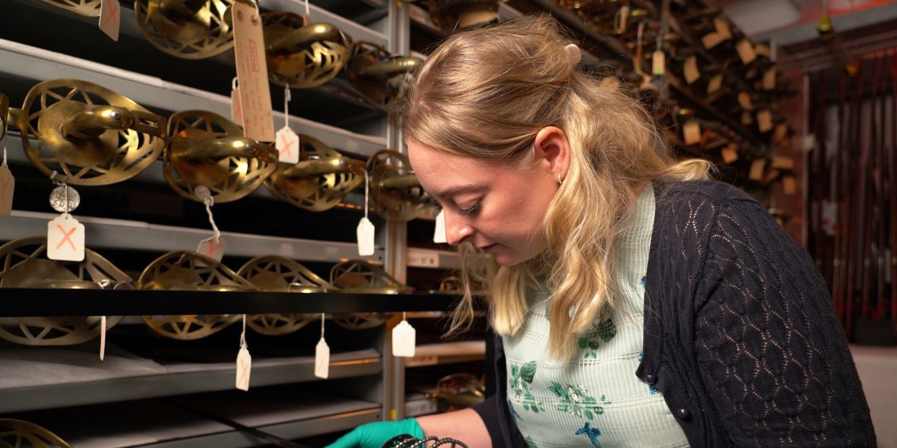 Curator wearing gloves examines a sword from a rack of swords
