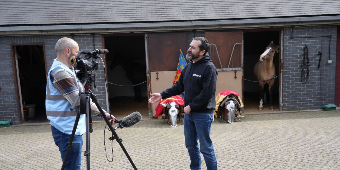 a horse watches from the stable as a member of staff is interviewed on camera