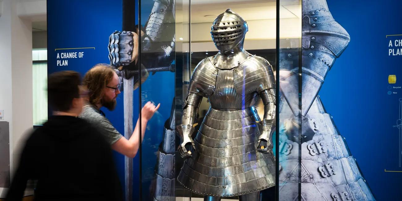 a couple stop to admire and examine a shining armour with a skirt that once belonged to Henry VIII
