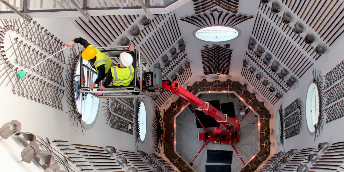 two people on a hydraulic platform wearing hi-vis vests while cleaning armour approximately 60feet up the hall of steel 