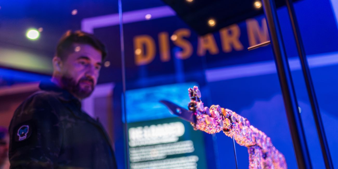 A man looking at an AK 47 gun covered in candy displayed in a glass case