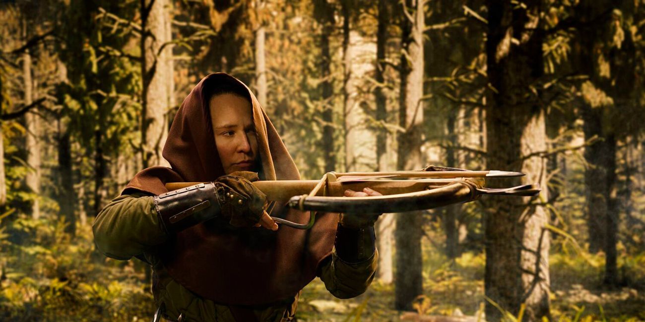 Person dressed in a hooded top holding a wooden crossbow in a forest