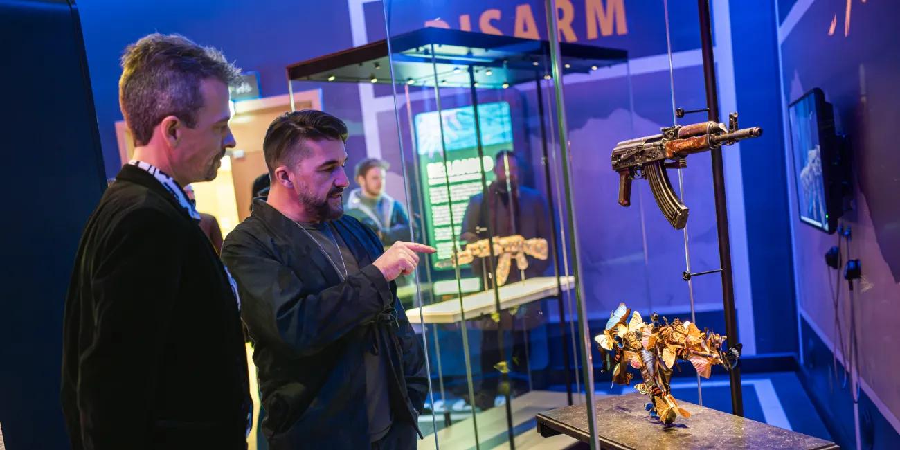 two people looking at two AK47 machine guns in a glass case