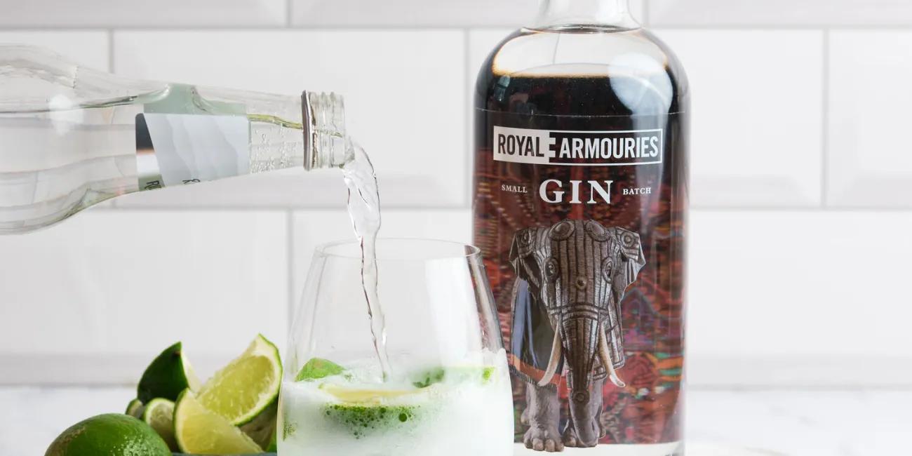 Royal Armouries GIN next to tonic being poured into glass with sliced limes.