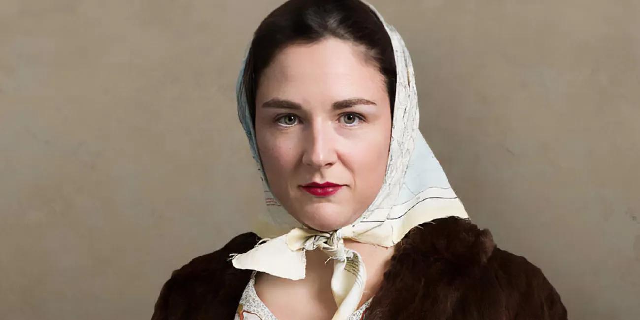 A young female SOE agent with a steely gaze poses in a fur coat and carries a sub-machine gun