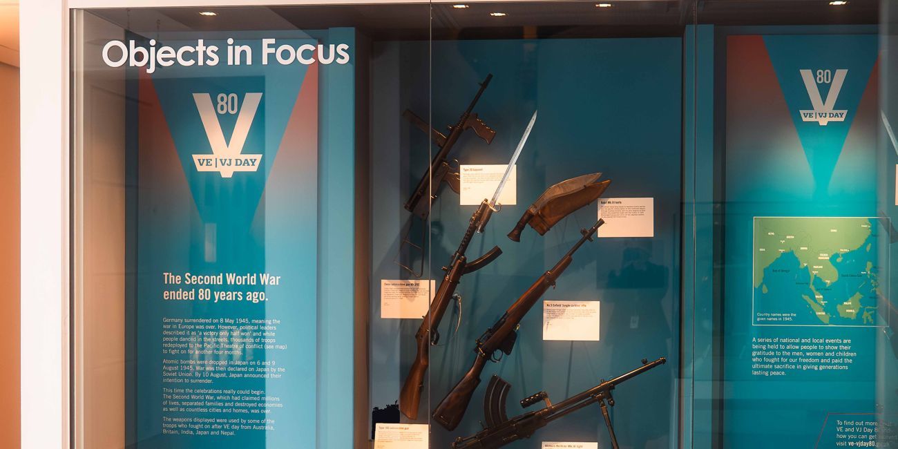 Display case featuring a collection of guns from the Second World War, text and photos about VE/VJ Day