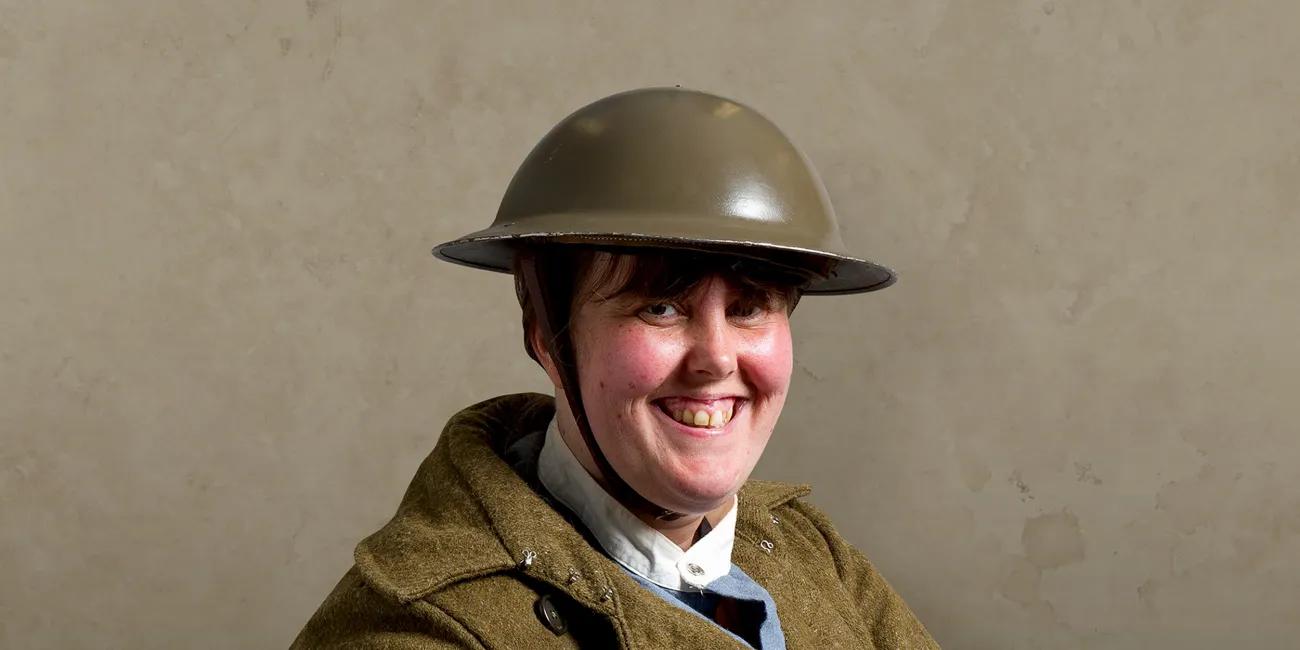 Woman wearing first world war tin helmet and khaki uniform and brown leather satchel