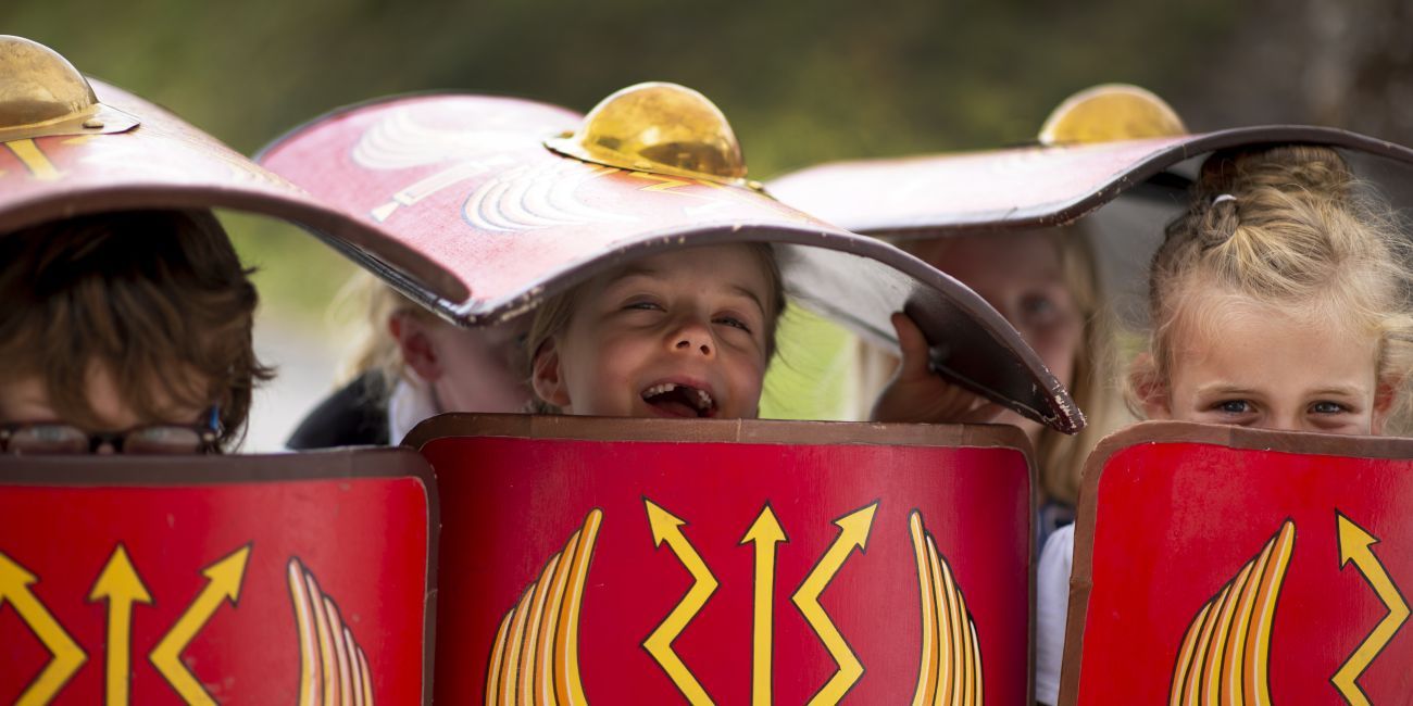 Three young children peeking out from under shields