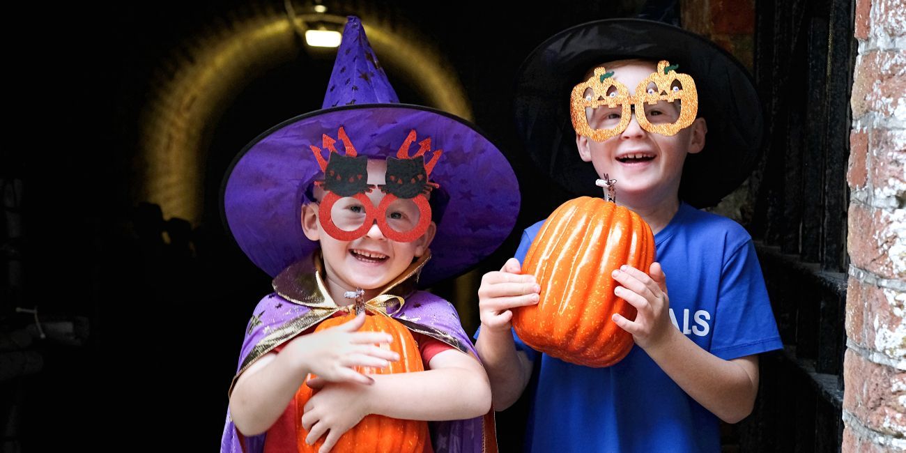 Two children in Halloween costumes with pumpkins