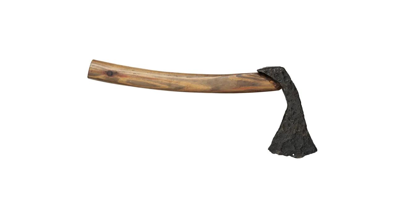 A weathered iron axe head with a rough, uneven surface fixed to a smooth, knot-marked wooden handle