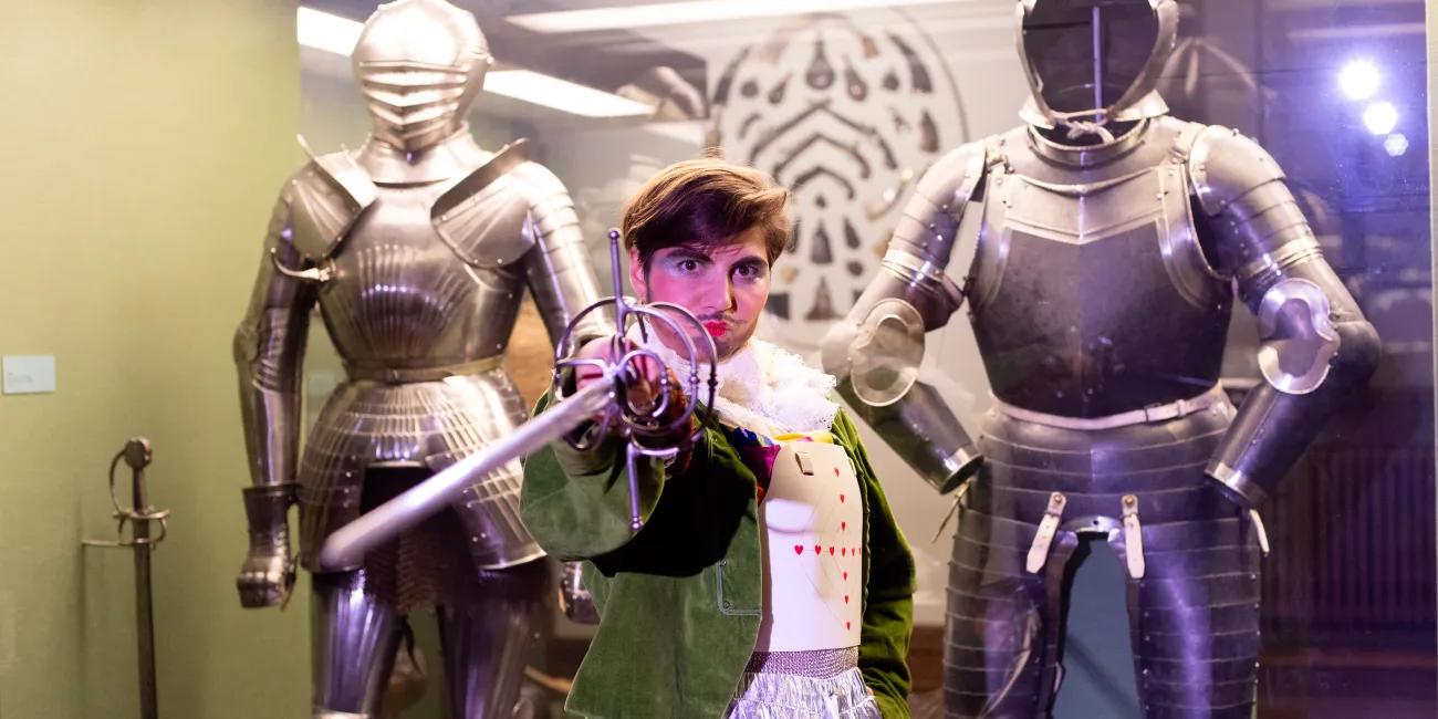 Person with sword standing between two suits of armour