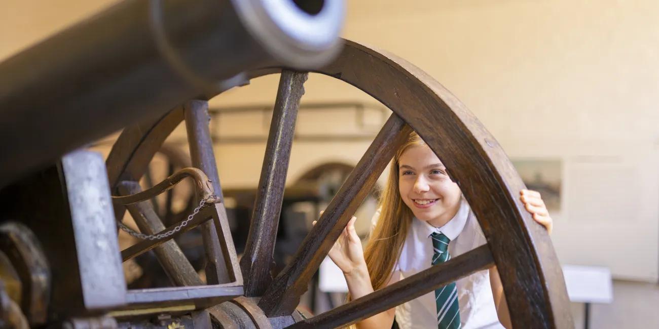 Student looks through the spokes of a wheel on an artillery piece. 