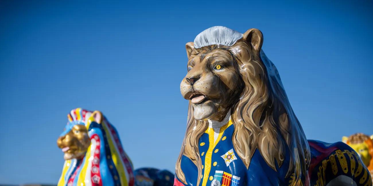 Decorated lion sculpture in a blue ceremonial uniform with medals, displayed outdoors against a clear blue sky