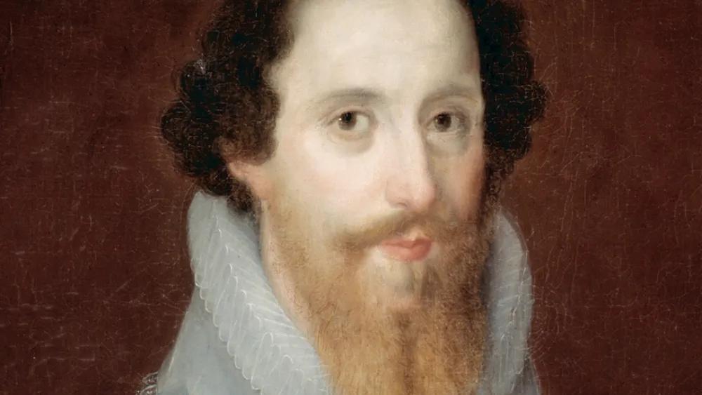 A close up portrait of a bearded man in a white 16th century ruff and mid-length brown hair.