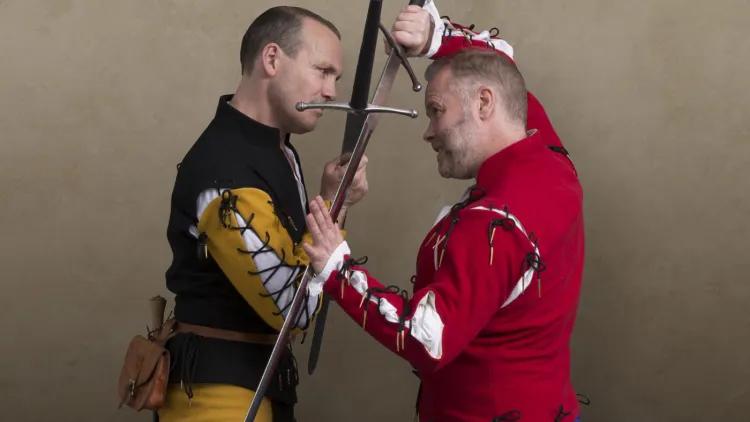 Two men in period costumes fighting with longswords