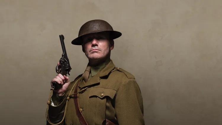 Man in khaki uniform and tin helmet holding a pistol