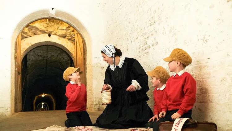 Florence Nightingale kneels on a bloodstained sheet with school children kneeling beside her