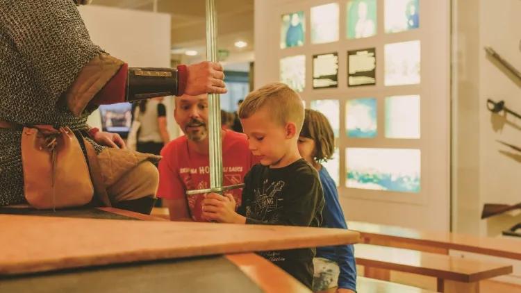 Museum staff member and child holding sword in an family activity at the museum