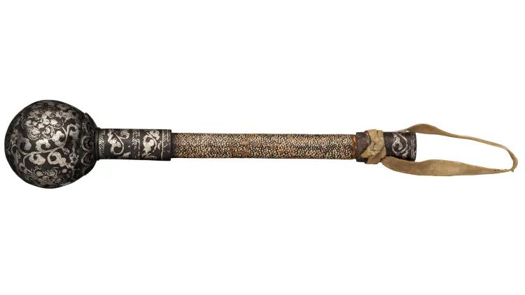Historical Mongolian mace with a patterned metal ball head, elongated grip wrapped in textured material, and a leather carrying strap, isolated against a white background