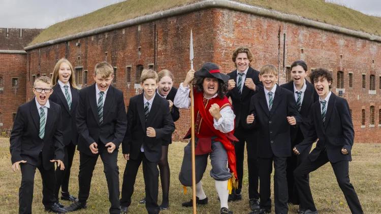 A man dressed as a Cavalier stands in the middle of a group of students. Everyone is shouting angrily. 