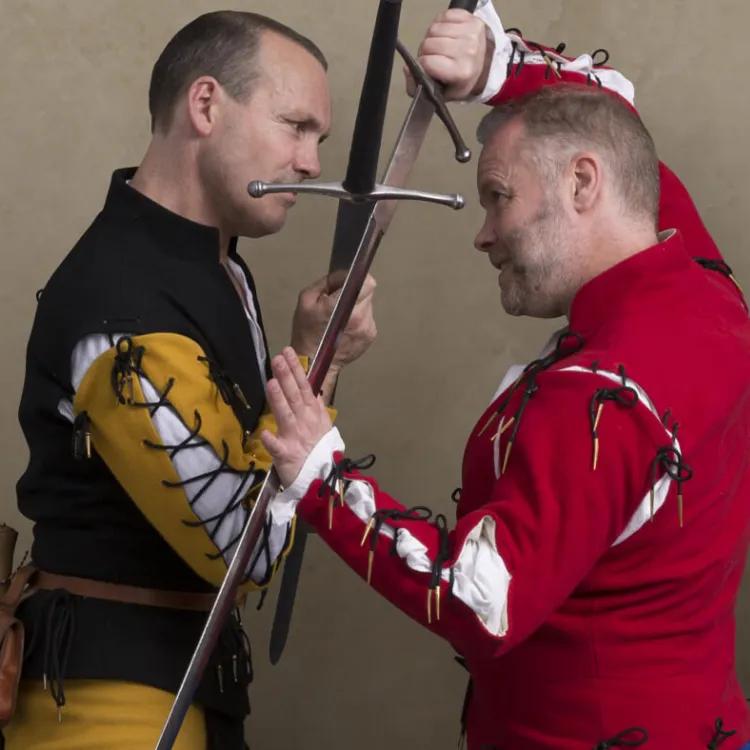 Two men in period costumes fighting with longswords