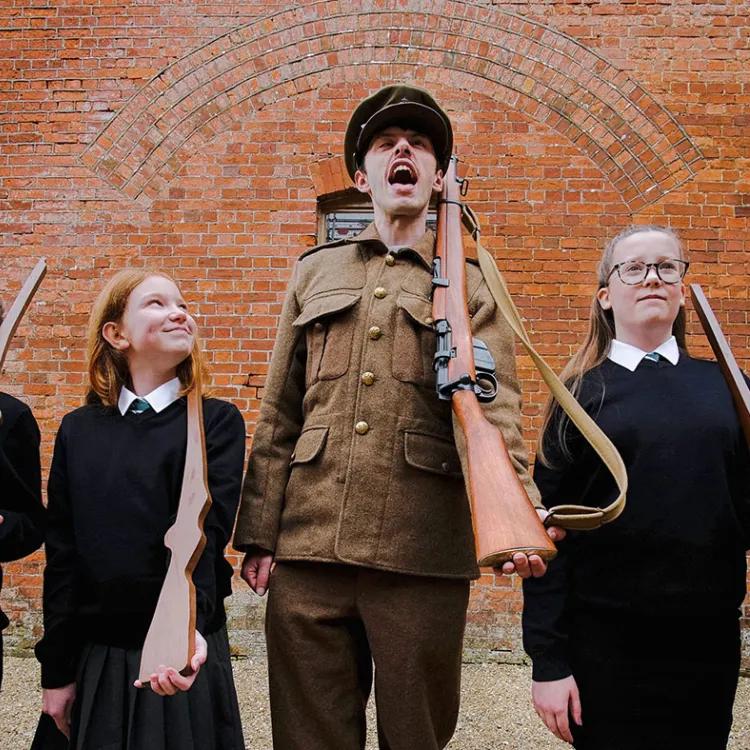Man in WW1 uniform shouts, four students stand either side of him looking forward, one looks up at him with a bemused expression