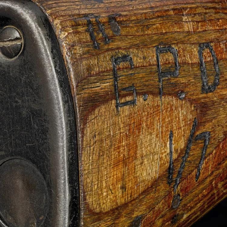 A close up of a wooden textured gun butt showing an engraving burned in to it