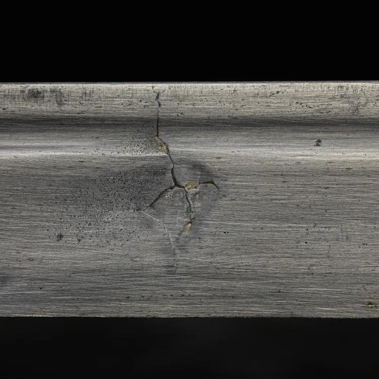 A close up of a silver sword with a crack in the middle on a black background