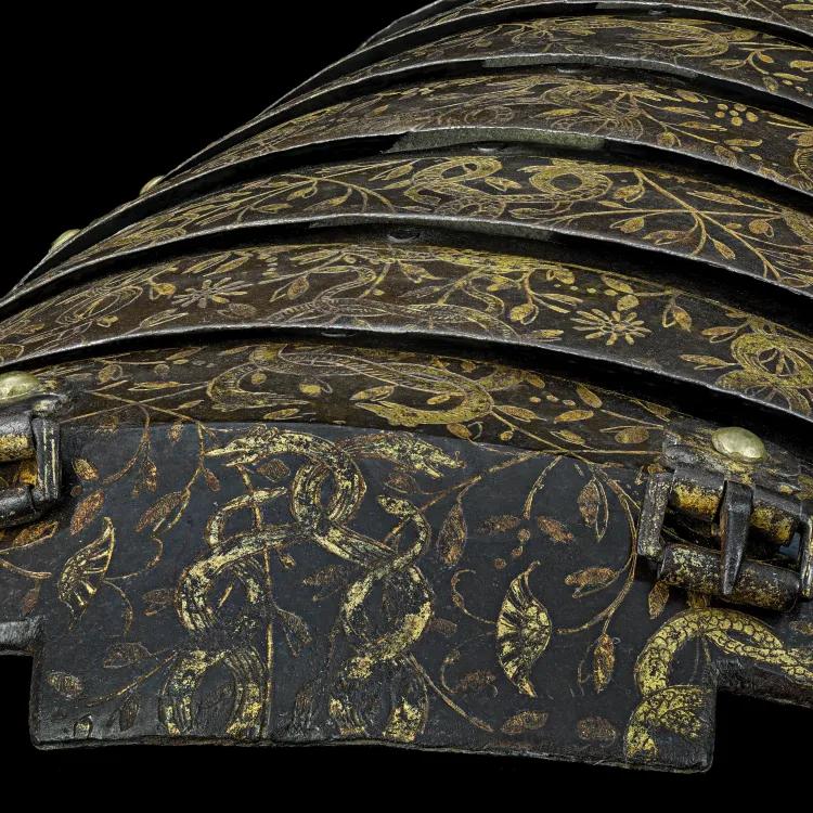 A dome shaped piece of armour decorated with buckles and gold foliage and animals 