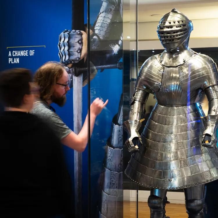 a couple stop to admire and examine a shining armour with a skirt that once belonged to Henry VIII