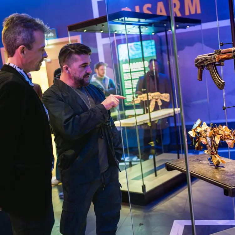 two people looking at two AK47 machine guns in a glass case
