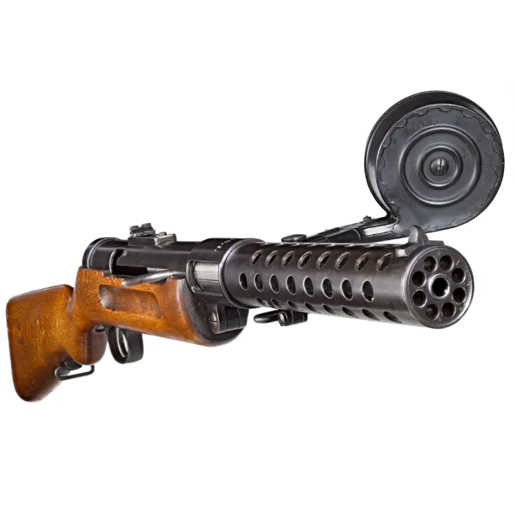 A black metal, perforated barrel attached to a short wooden stock and a drum magazine attached to the side