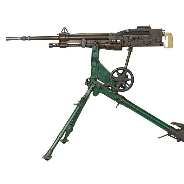 A slim barrelled St. Etienne machine gun with bronze/brass grips mounted on a green tripod