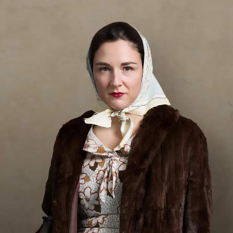 A young female SOE agent with a steely gaze poses in a fur coat and carries a sub-machine gun