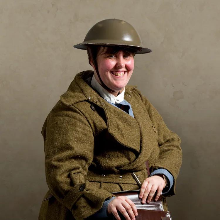 Woman wearing first world war tin helmet and khaki uniform and brown leather satchel