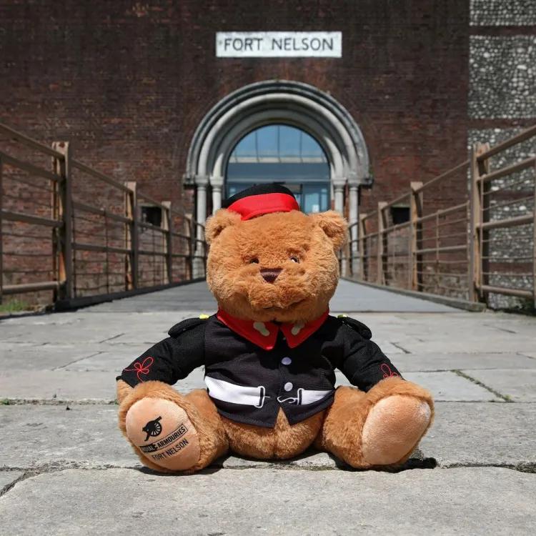 Brown teddy bear dressed in Victorian military uniform sitting in front of the entrance to Fort Nelson
