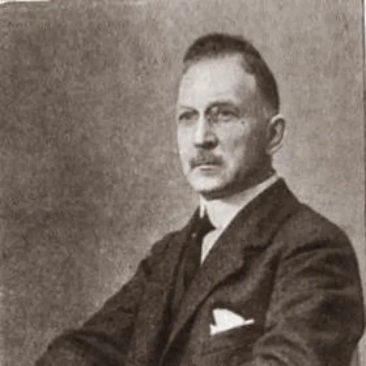 A sepia tone photo of a seated, moustached man in a suit