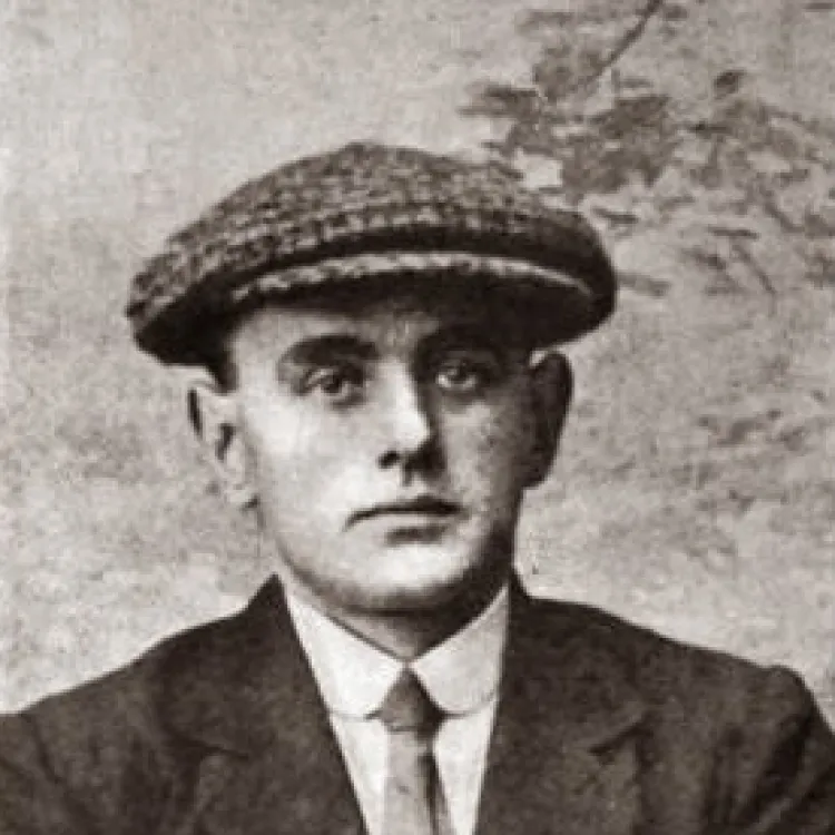 A black and white photo of a man dressed in a flat cap, suit and tie.