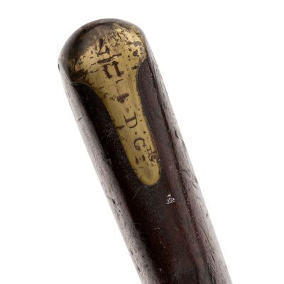 A brass plate attached to the buttstock of a carbine, engraved with the number 4 and 11, and the letters D and G.