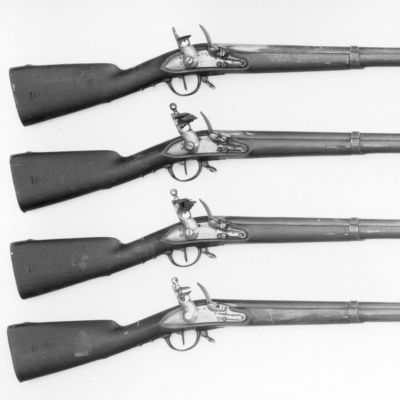 A black and white photo of four muskets finished in wood and iron, bound by three bands each with raised foresight